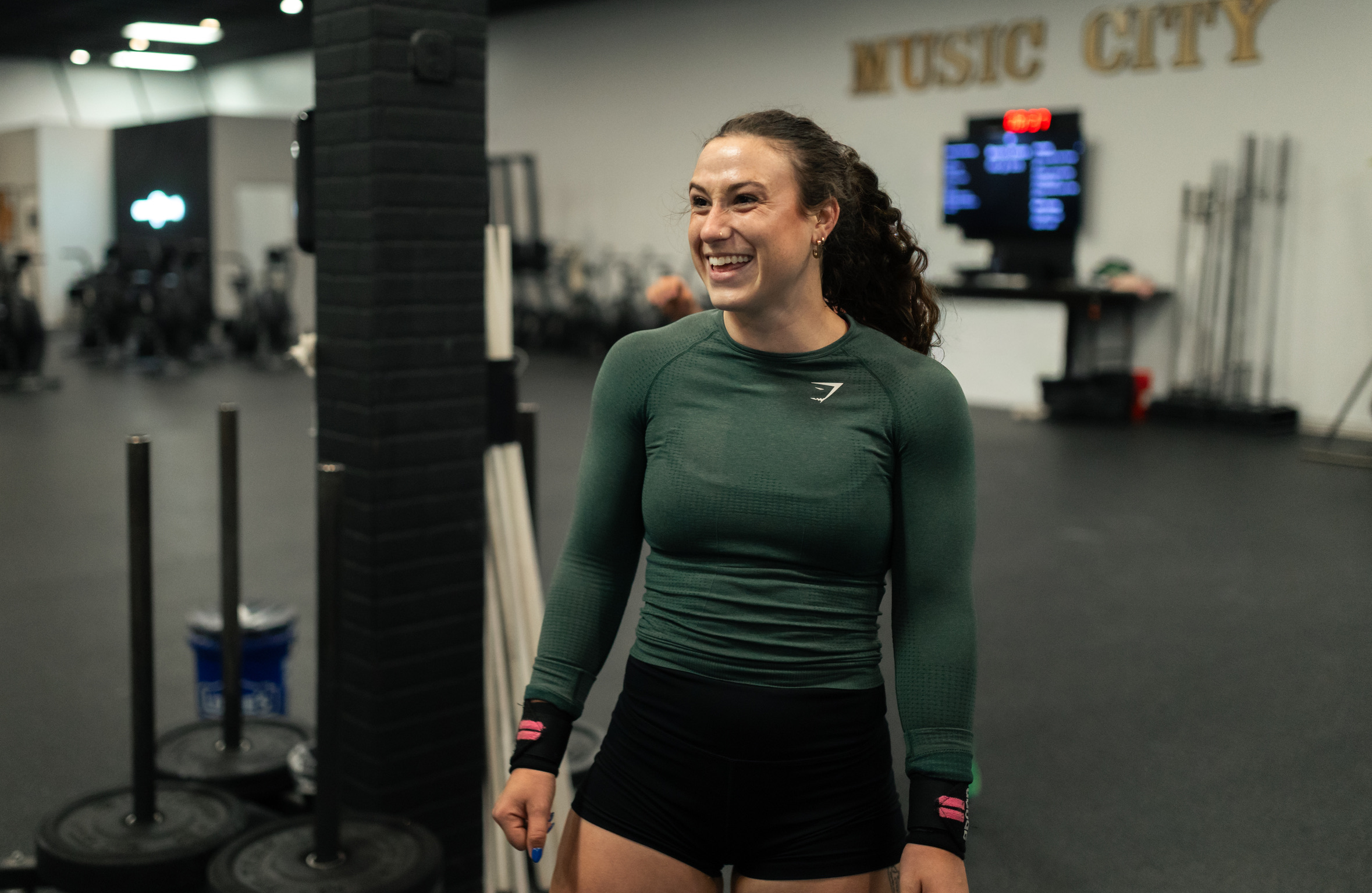 Member smiling on the gym floor in front of the Music City wall